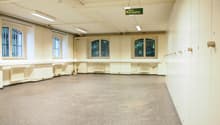 Large open room with high ceilings, arched windows, and a 'Not ausgang' (emergency exit) sign. The room has a concrete floor and appears to be a multipurpose space, possibly used for events or activities.