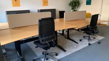 Empty office space with desks, office chairs, wall-mounted frames, and a potted plant.