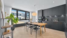 dining area with wooden table, black chairs, kitchen with black cabinets, kitchen island, plant, view of outside