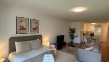 a bedroom with a large bed, two nightstands, a couch, a television, a microwave, a desk, and a dining table with chairs