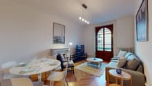 white painted walls, white hardwood floors, a fireplace, a large glass door with a window, a round wooden coffee table, a rug, a grey sectional sofa, a dining area with a round white table and chairs, a TV with a TV stand, a side table with a bowl, a lamp