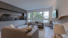 Spacious living room with two sofas, coffee table, mounted TV, large windows with trees view