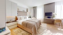 A bedroom with a wooden floor, a large bed with pillows, a desk with a TV, and a white cabinet.