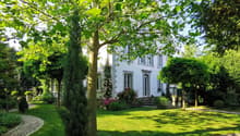 2 story house, white exterior, surrounded by green lawn, flower garden, trees, pathway