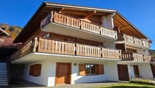 Two story house, wooden balcony, red roof, two doors, one window, garden