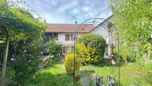 well-maintained garden with various plants, trees, shrubs, pathway, metal arch, patio set, metal trellis, and a house in the background