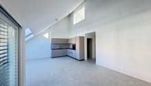 Empty room with white walls, gray floor, kitchen area with cabinets, sink, and oven, glass door, skylights