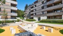Multi-story apartment buildings with wooden facades, balconies, and a landscaped courtyard with a modern sculpture and seating area.