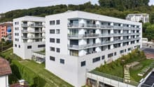 White apartment building, multiple balconies, multiple windows, surrounded by green landscape