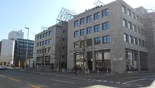 Commercial building, glass windows, grey walls, multiple floors, people walking, street lights, parked car