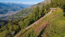 A small chalet on a hill with view of valley and mountains.