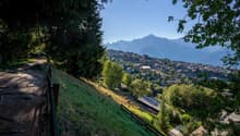 hillside path, grassy area, trees, village houses, mountains in background