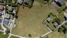 Aerial view of a plot of land with surrounding houses and green areas.