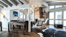 beamed ceiling, wooden floor, fireplace, sofa, coffee table, chess board, two armchairs, carpet, desk, picture on wall