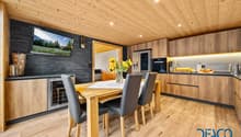 wooden floor, wooden wall, TV, wooden dining table, black chairs, wooden cabinets, refrigerator, oven, countertop with flowers, toaster, wine rack