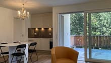 dining area with a round table, chairs, and chandeliers, a brown chair, a wooden table with a decorative piece, an open kitchen, and an exit to the balcony