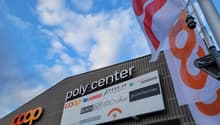 Commercial building with a large sign reading 'poly center', multiple logos on the sign, and flags on poles