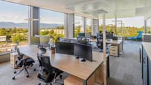 Large windows, desks, monitors, office chairs, trees and mountains view outside