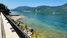 Pathway with railings, rocky shore, clear water, mountains in the distance