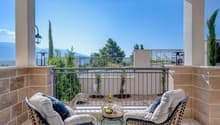 two wicker chairs with cushions, small table with wine bottle and grapes, railings, sunny view of mountains