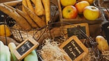 Various fresh produce including parsnips, apples, potatoes, leeks, and lemons in baskets with wooden labels