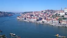 Aerial view of the historic city of Porto, Portugal, situated along the Douro River. The city is characterized by its colorful buildings, winding streets, and iconic bridges spanning the river.