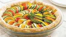 Colorful vegetable tart or quiche with sliced zucchini, tomatoes, and other vegetables arranged in a pie crust