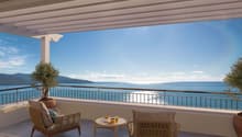 Spacious balcony with panoramic view of the sea, mountains, and blue sky. Furnished with comfortable wicker chairs and a small table, providing an ideal spot to relax and enjoy the scenic surroundings.