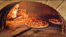 A traditional brick pizza oven with a fire burning inside, and two freshly baked pizzas on the oven floor