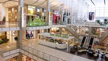 Large indoor shopping mall with multiple levels, glass walls, and various retail stores and shops visible.