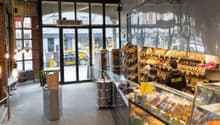Bakery shop with glass display case, shelves, bread and pastries, tables and chairs, lamps, trash bin, and a trash chute.