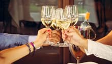 A celebration with four wine glasses raised and a bottle of wine on ice.