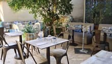 Outdoor seating area with tables, chairs, umbrellas, plants, and a chalkboard menu.