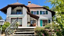2 story house, red brick, white windows, red roof, garden, balcony, elevated ground floor, flowers, outdoor table and chairs