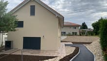 Modern 2 story house, beige, with garage, concrete driveway, gravel path, solar panels on the back house.