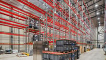 large warehouse with red and silver metal shelving, multiple stacked boxes, large silver refrigerator, concrete floor