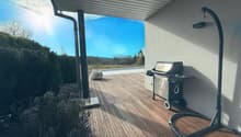 Covered outdoor patio with wooden deck, gas grill, and a view of the swimming pool and surrounding landscape.