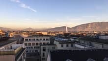 Cityscape with multiple buildings, mountains in the background, and a fountain in the distance