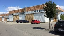Industrial building with multiple windows, cars parked in front, tree in front