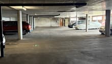 Indoor parking garage with concrete floor, concrete ceiling, and several parked cars