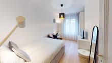 Spacious bedroom with white walls, hardwood floors, large window, pendant light fixture, and decorative accents.