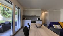 modern kitchen with dining area, large windows, wooden floor, white cabinets, modern appliances, dining table, chairs, couch with pillows