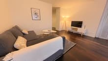 Living room with a gray sofa, two white pillows, a white coffee table, a floor lamp, a flat screen TV, a white entertainment center, a picture frame on the wall, and a rug.