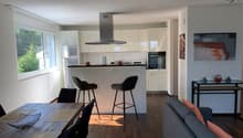 Open kitchen with dining area, living room with couch, dining table, chairs, kitchen island, bar stools, kitchen appliances, window, paintings on wall