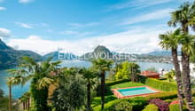 Luxury villa with swimming pool, surrounded by lush tropical gardens and palm trees, overlooking a scenic lake and mountains in the background.