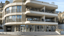 Contemporary multi-storey building with a curved facade, several balconies, glass railings, and a modern glass entrance.