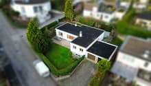 Detached house, single story, white walls, brown garage, paved driveway, garden, hedges, green grass, asphalt road