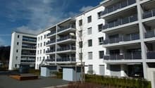 Multi-story apartment building with balconies, surrounded by landscaping and paved areas