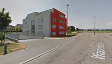 Modern building with red and white facade, located on the corner of a street, surrounded by greenery and a parking lot