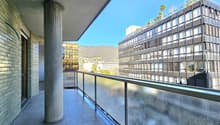 Balcony with glass railing, tiled floor, pillar, view of a building and mountain
